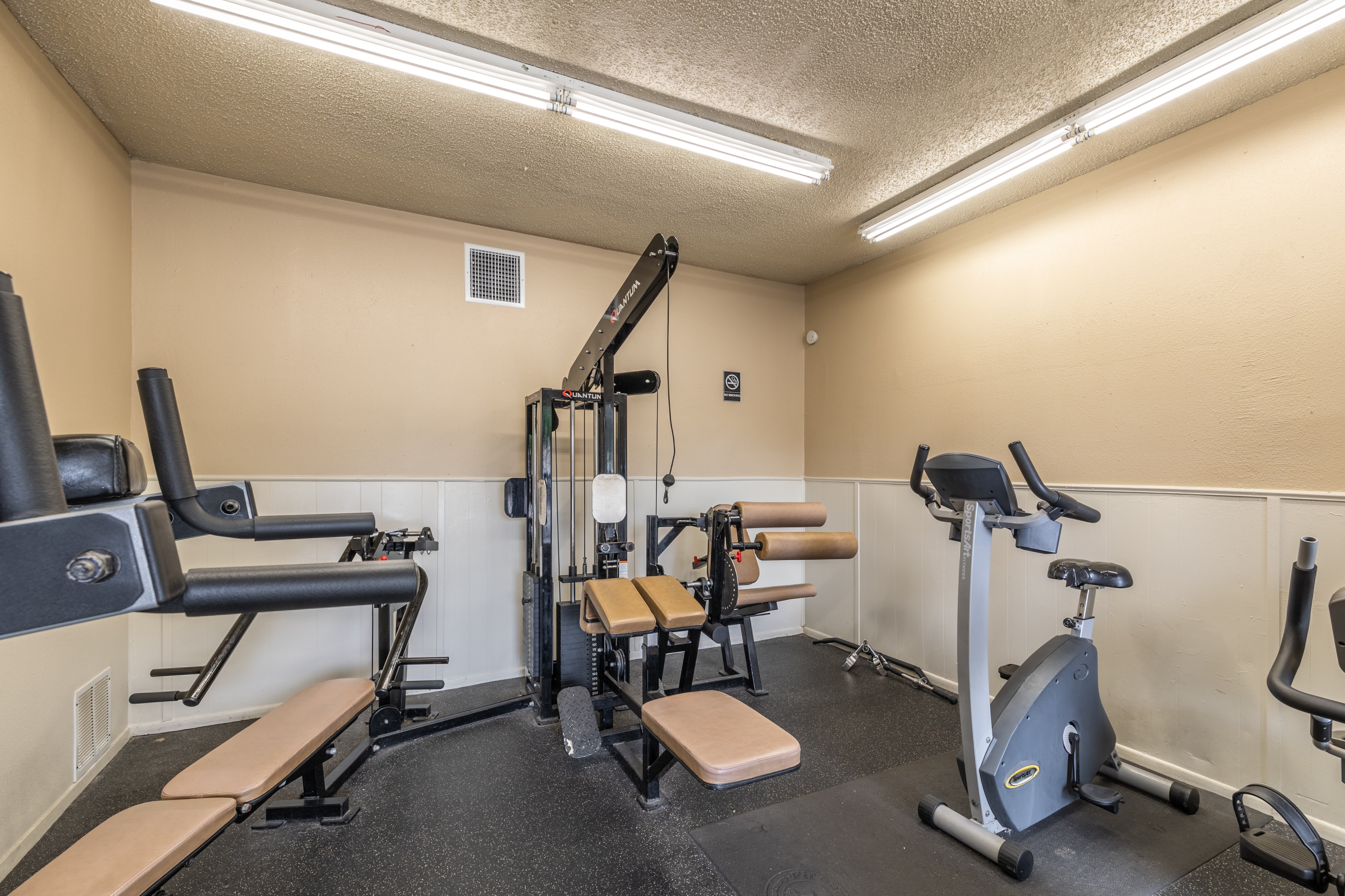 A gym with a variety of equipment including a treadmill, weights, and a bench.